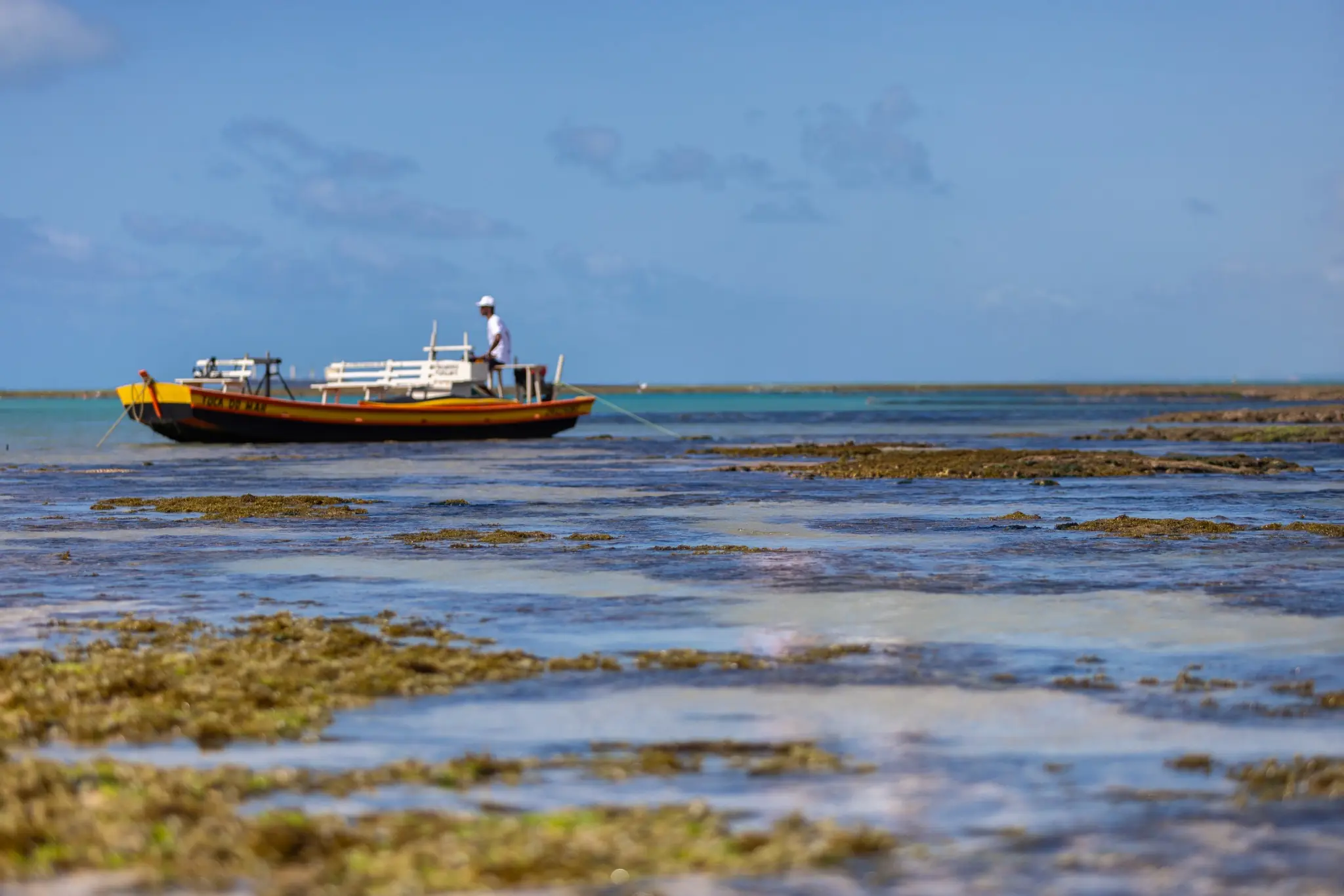 Piscina natural da Pajuçara com jangada e jangadeiro ao longe, em Maceió