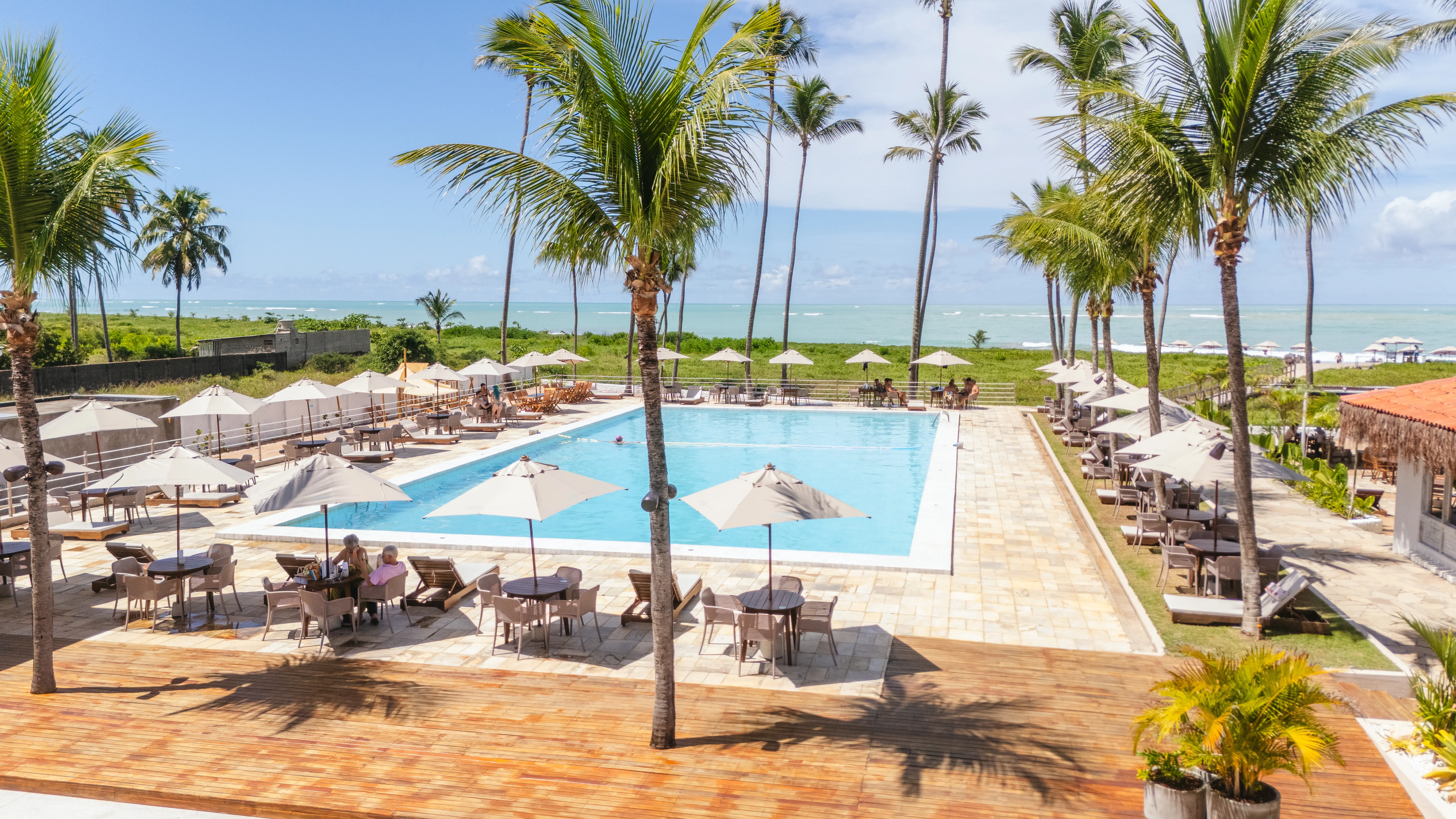 Vista aérea próxima da piscina, dos ombrelones e coqueiros do Vivari Beach Club