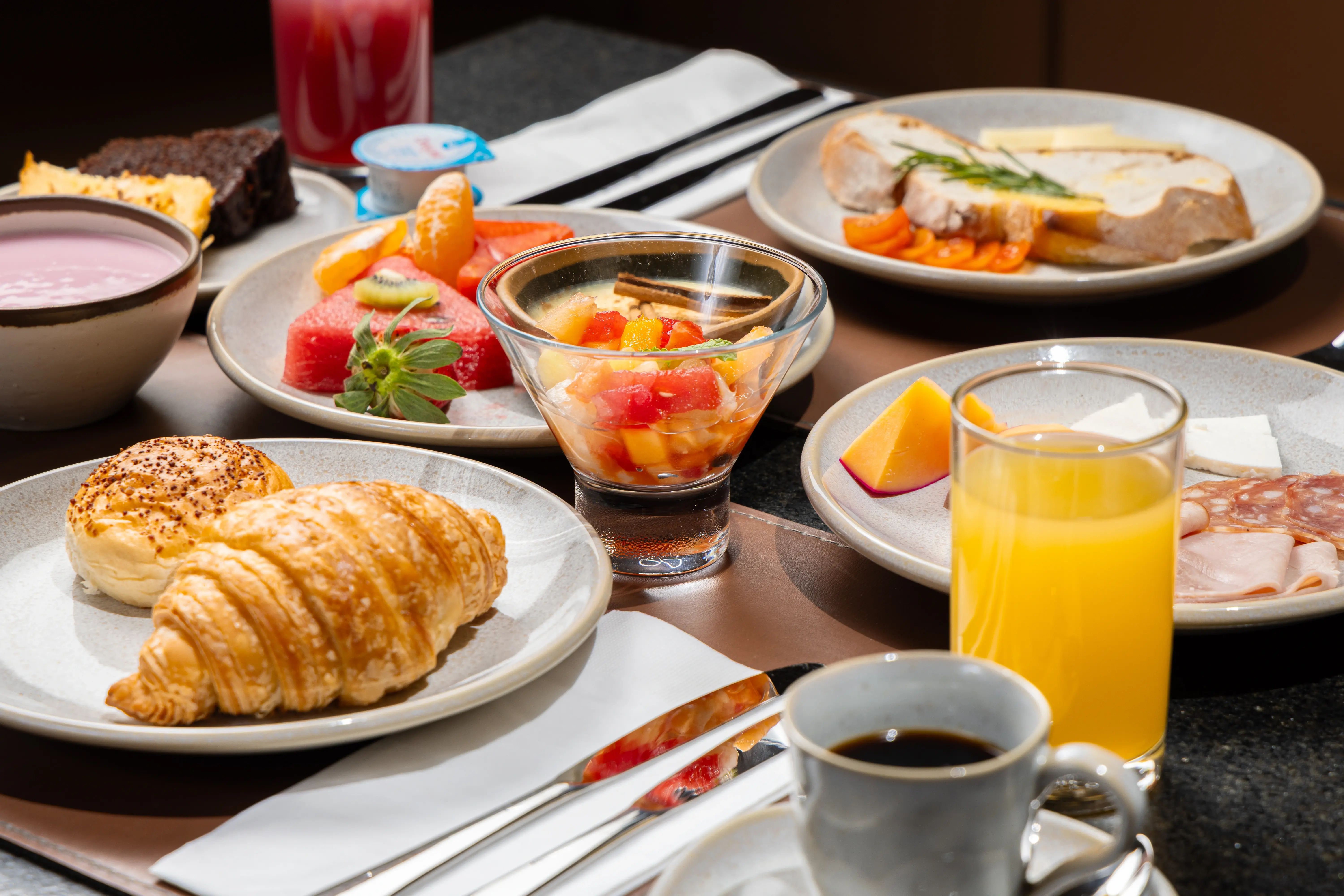 Mesa de café da manhã com frutas, croissant, suco e café