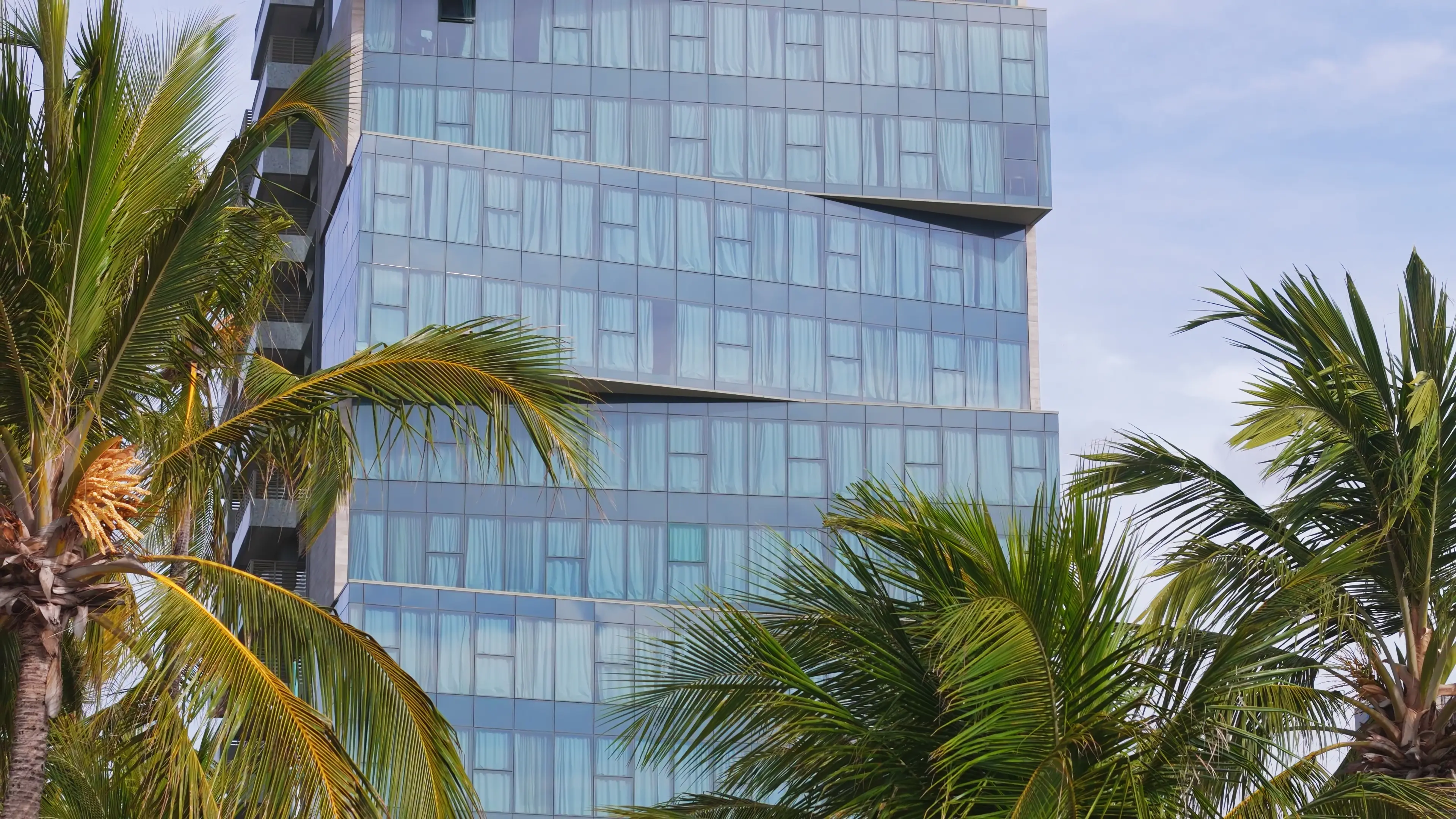 Fachada do Sais Beach Living Hotel com coqueiros à frente, em Maceió