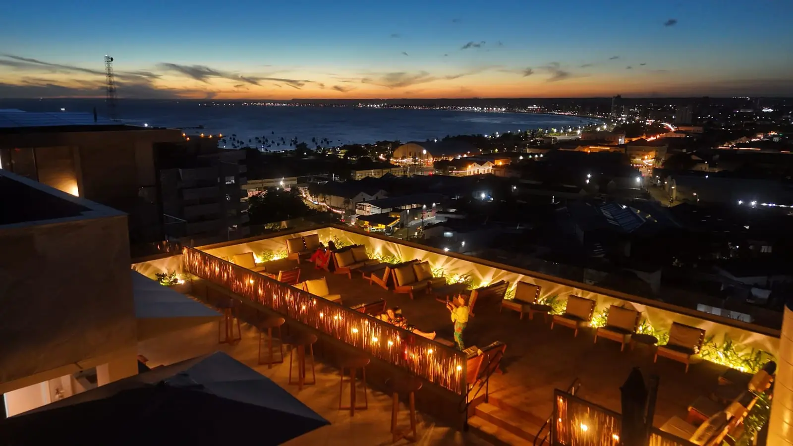 Poltronas do sunset deck com o pôr do sol ao fundo, no rooftop do Sais Beach Living